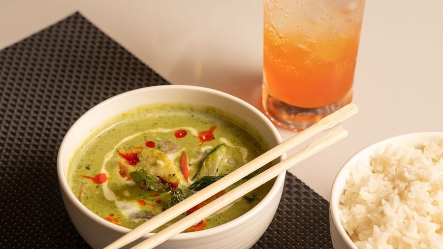 A glass of juice, a bowl of soup , and a bowl of rice kept on a white table at Ananta Spa and Resort, Ajabgarh
