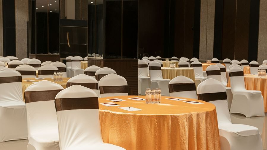 A hotel event space set with orange and white draped tables and chairs - Biznotel By Pride Surat