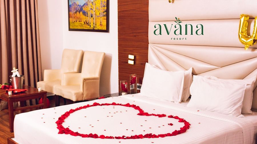 A hotel room decorated for a romantic occasion, with a heart-shaped rose petal arrangement on the bed and LOVE balloons.
