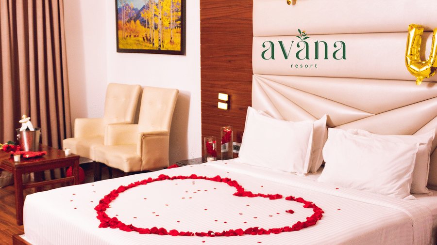 A hotel room decorated for a romantic occasion, with a heart-shaped rose petal arrangement on the bed and love balloons.