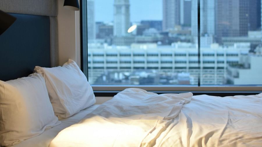 A modern hotel bedroom with a large window offering a cityscape view and a comfortable bed.