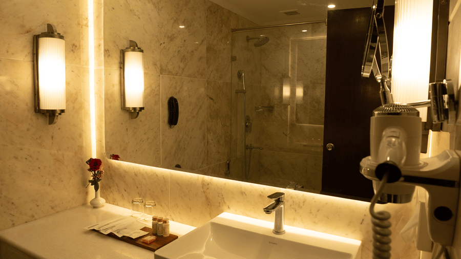The Deluxe King bathroom at Clarks Amer, Jaipur features marble walls and a modern vanity with integrated lighting.