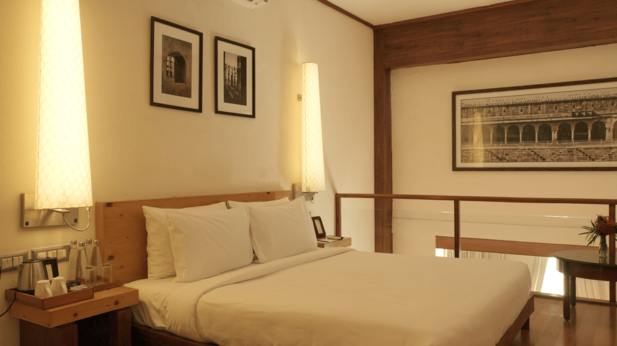 A bedroom with a king size bed, bedside tables, wall-mounted artwork, and wooden flooring in the Penthouse Suite at Clarks Amer, Jaipur.