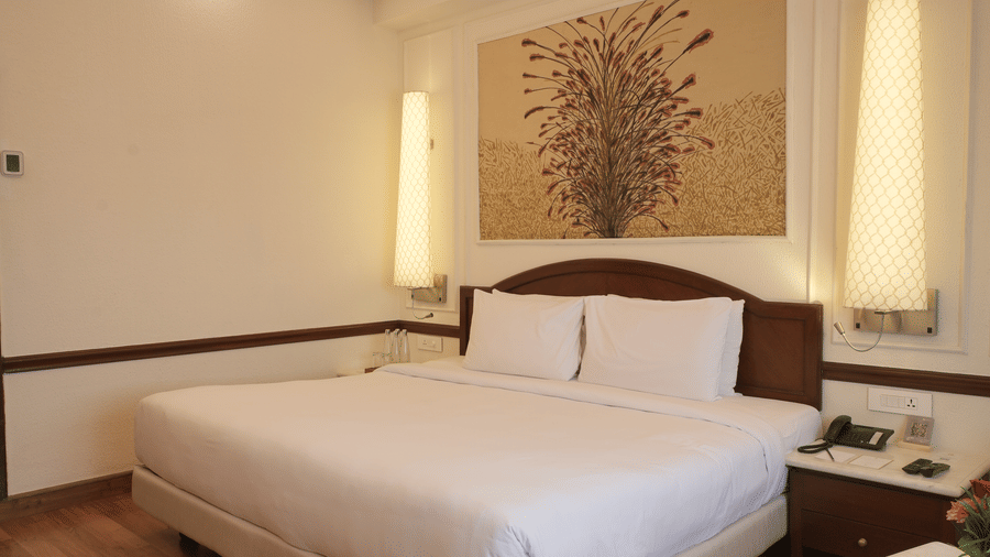 The Superior King bedroom at Clarks Amer, Jaipur includes a large bed, hardwood floors, and a decorative ceiling light fixture.