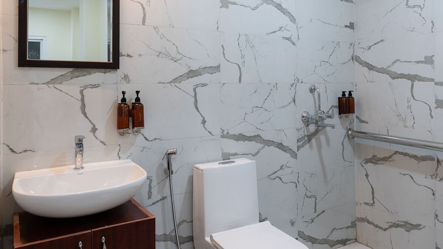Bathroom at Clarks Inn, Near Kainchi Dham features a white toilet and sink with a dark wooden cabinet, a mirror, and a shower area with marble-effect tiling