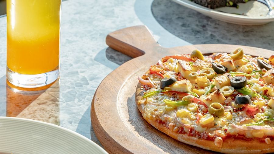 Assorted desserts and beverages including pizza slice, cake, soup bowls and juice on grey marble surface at Clarks Inn Suites, Hyderabad
