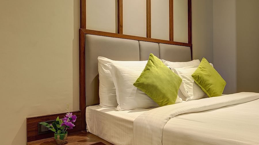 A double bed with side table next to it inside Classic AC Room - Fortune House, Magarpatta