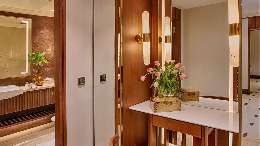 An elegant bathroom featuring a large vanity with a mirror, modern fixtures, a marble countertop, a cushioned stool, and warm ambient lighting