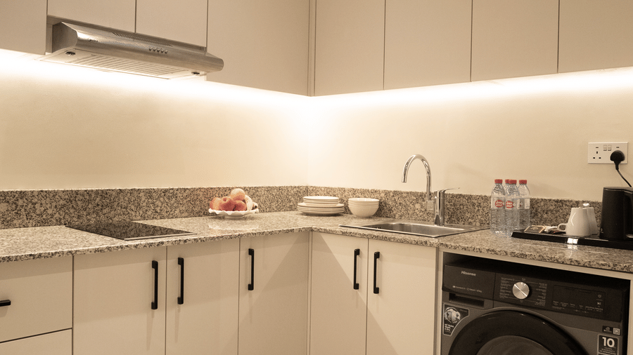 Modern white kitchen with granite-look counters, integrated washing machine, stainless steel range hood, and under-cabinet lighting.