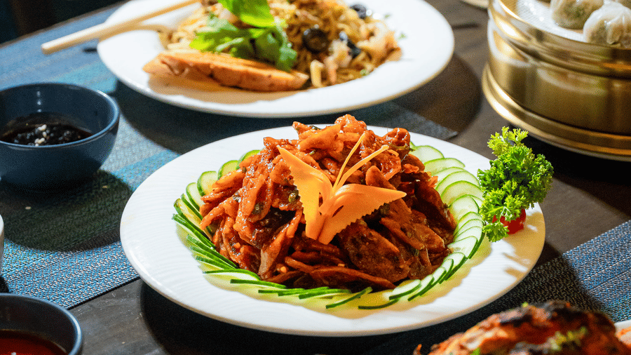 Plated dishes at Nirvana Sarovar Portico, Gorakhpur featuring cooked meat, dim sum in a basket, and vegetable sides.