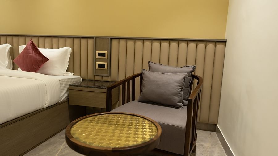 A cosy corner in a room at Pride Resort, Jodhpur, featuring a cushioned chair and a small round table beside the bed.