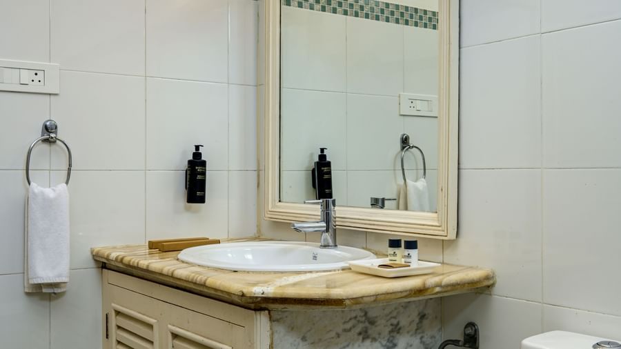 A bathroom at Ram Pratap Palace, Udaipur, featuring a storage cabinet, a mirror, a sink, a western toilet, and essential toiletries.