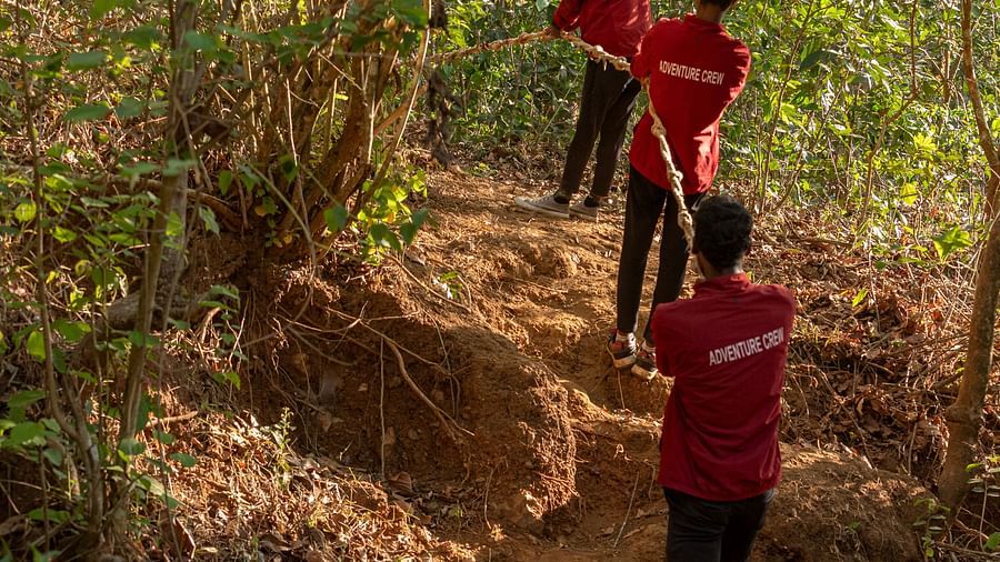 Three people hiking through a dense forest trail in red shirts. | Stone Wood Jungle Resort, Dandeli
