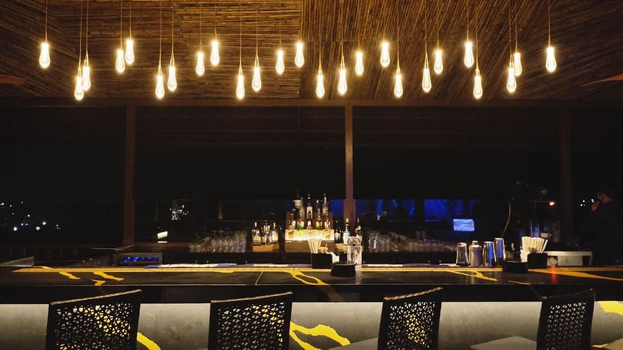 bar stools next to the bar counter with a big chandelier in the roof - Ananta Udaipur