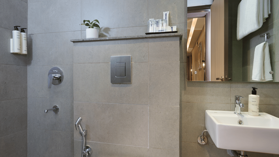 A modern bathroom at Tulip Inn Gurugram with stone tiling, a wall-mounted commode, and a small vanity sink with a mirror.