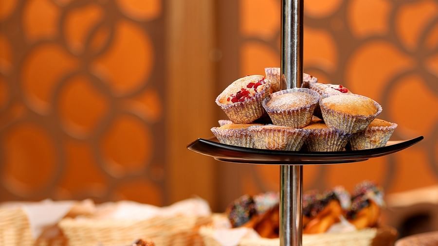 An assortment of muffins, cupcakes, and desserts neatly arranged in baskets on a table at Uday Backwater Resort, with a tong placed beside them