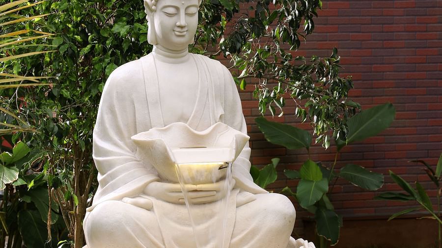 A serene white Buddha statue in a meditative pose, placed on the lush lawn at Uday Backwater Resort