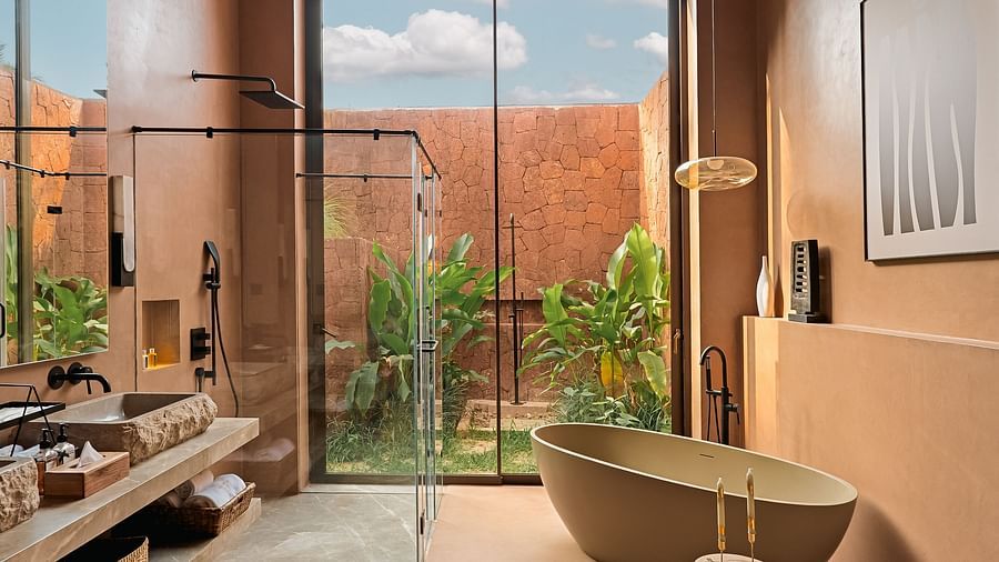 A modern bathroom at Villa Moira by V Escapes, showcasing a freestanding bathtub, an outdoor shower area, and large windows with garden views.