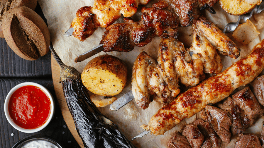 Gourmet barbecue feast with grilled meat skewers, dips, and traditional sides beautifully presented on wooden table.