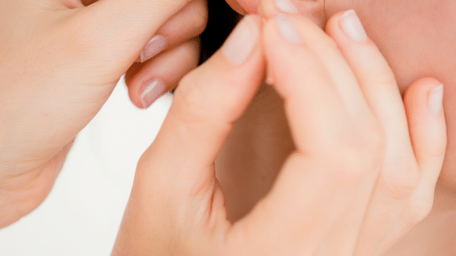 A pair of hands gently holding the earlobe of a person for auricular acupuncture at YO1 Longevity & Health Resorts