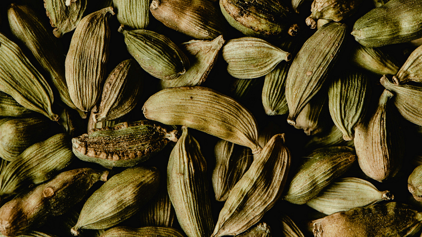 Green cardamom pods tightly packed, filling a narrow vertical frame, showing texture and detail.