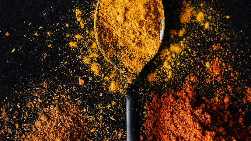 Spoon with yellow powder (turmeric) on dark surface, surrounded by red and orange spices.