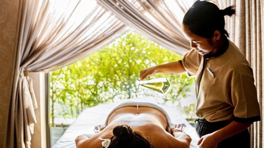 A spa therapist giving an oil massage to a guest who is lying down on a table in a room.