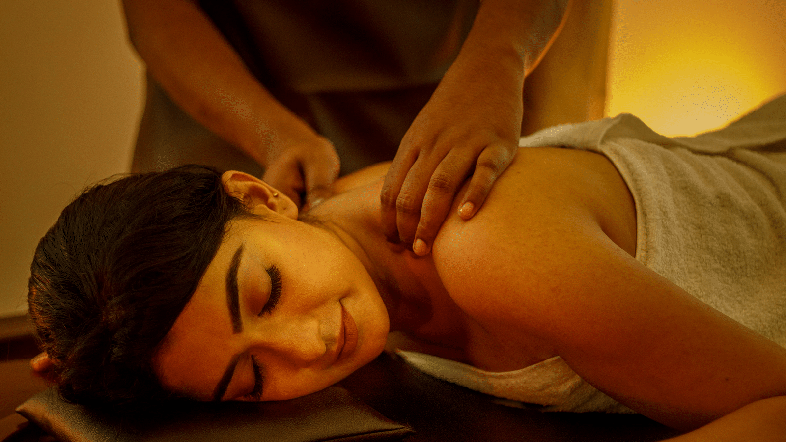 A person receiving a head massage while lying on a massage table, in a dimly lit setting with a candle.