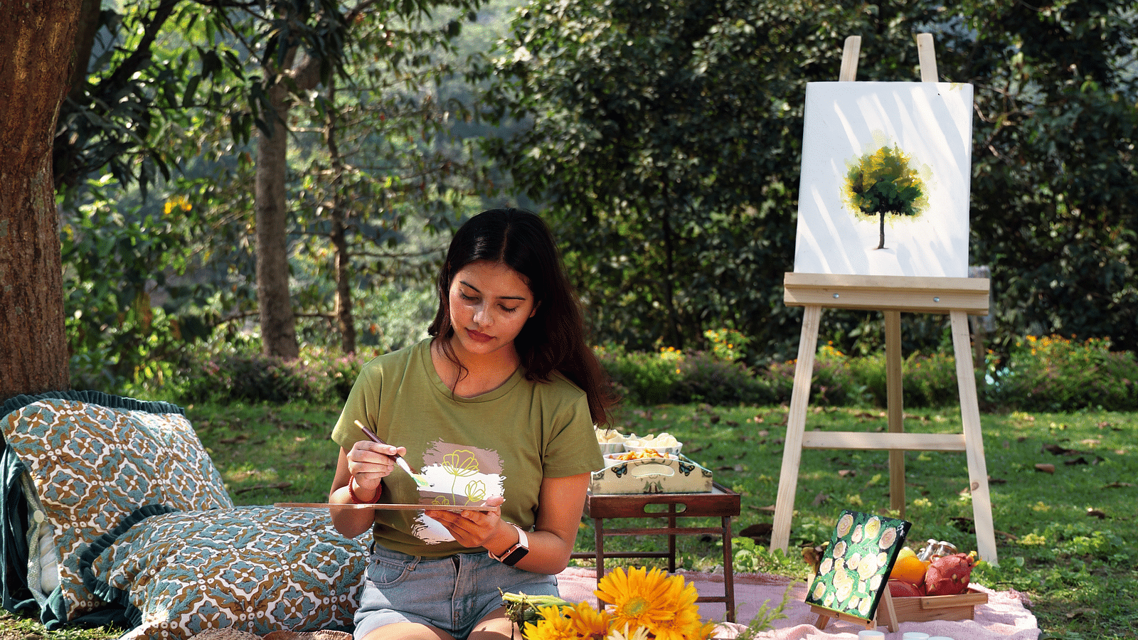 A woman sitting on a picnic mat painting at the Sylvan Retreat, Dehradun.