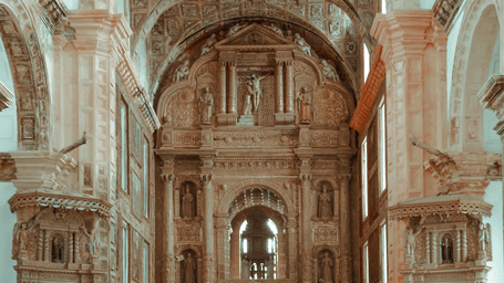Well-lit interior of the Basilica of Bom Jesus, Goa, featuring intricate details of the carvings on the ceiling, walls, and walls at the altar