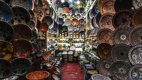 A narrow aisle in an Oriental shop, filled with colorful bowls, plates, and hanging lamps, creates a vibrant and immersive shopping experience.