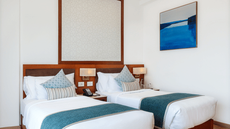 A well-lit hotel room arranged with 2 single beds, a wall painting, and a warm recessed ceiling border at Tiara by MPS.
