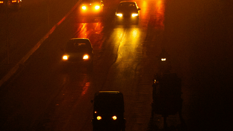 Night-time aerial view of a busy road illuminated by glowing streetlights, with vehicles travelling through the surrounding darkness