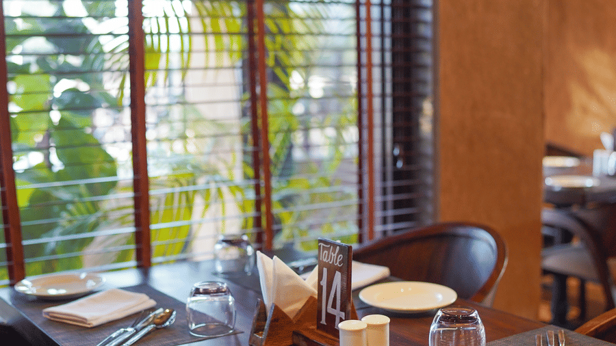 A dining table set for a meal, positioned by window blinds, at Aamaghati Wildlife Resort.