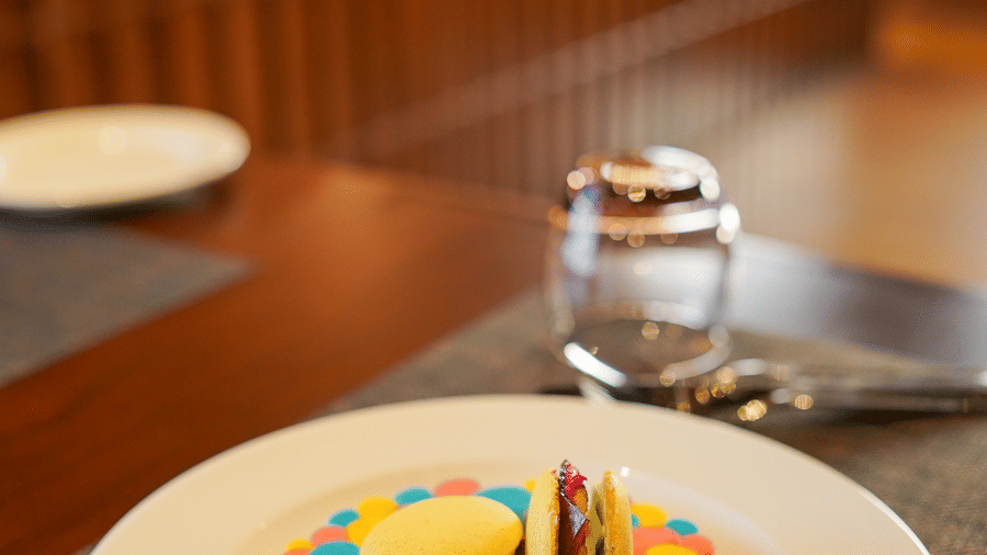 A colourful dessert presented on a white plate with a drink in the background at Aamaghati Wildlife Resort.