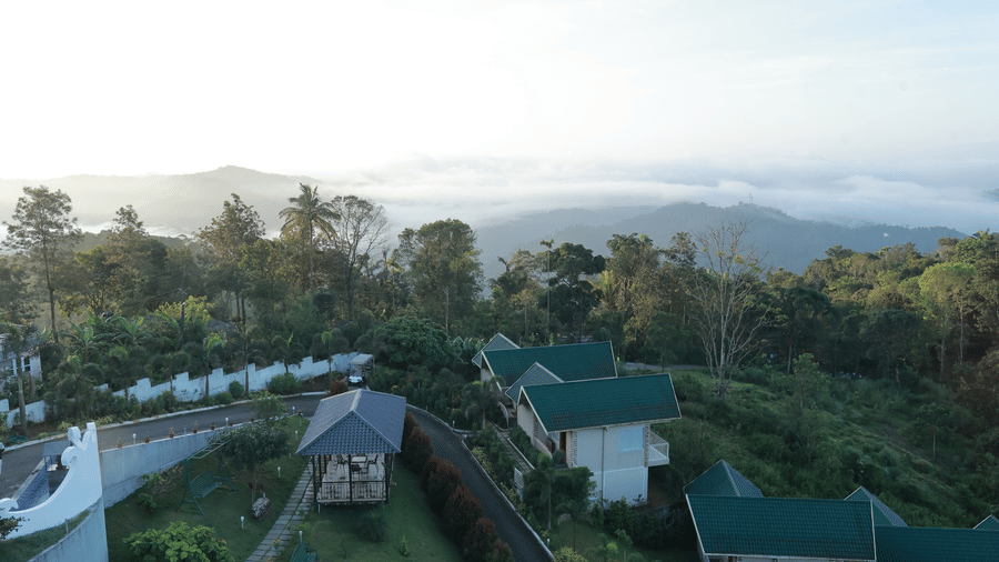 A wide-angle shot of Aveda Mountains and Mist Resort and Spa, Munnar, overlooking the misty mountain valleys illuminated by the bright sunshine.