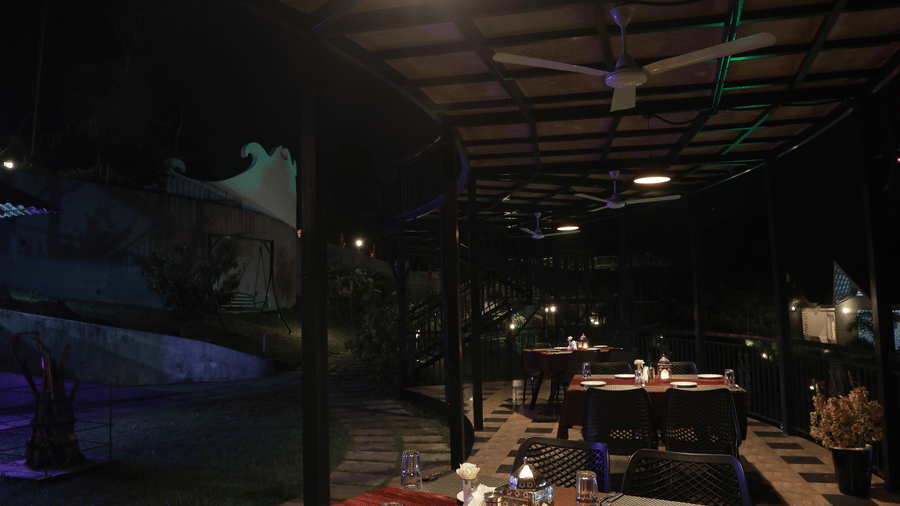 A well-arranged dining table with table mats and cutlery at the Machaan restaurant under a outdoor lanp hanging from the ceiling at Aveda Mountains and Mist Resort and Spa, Munnar.
