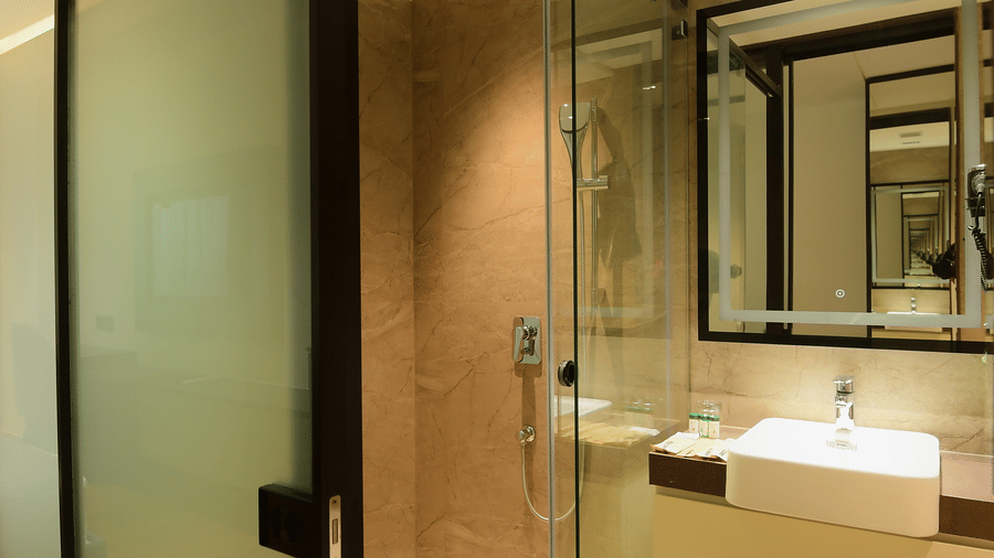A bathroom glass shower cubicle next to a vanity counter with a washbasin, and a mirror at Awesome Palace, Guwahati Airport.