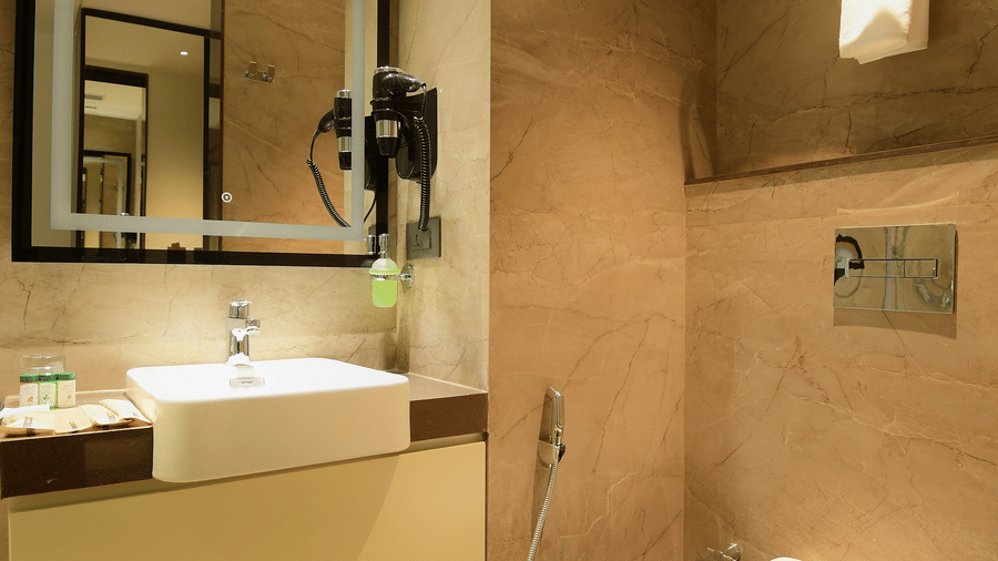 A bathroom featuring a washbasin counter, an illuminated mirror, and a toilet at Awesome Palace, Guwahati Airport.