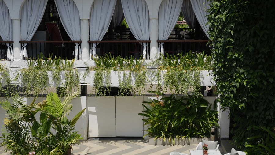 An open courtyard with patterned tiling, white outdoor tables, and sun loungers next to a building facade at Bougainvillea, Alibaug.