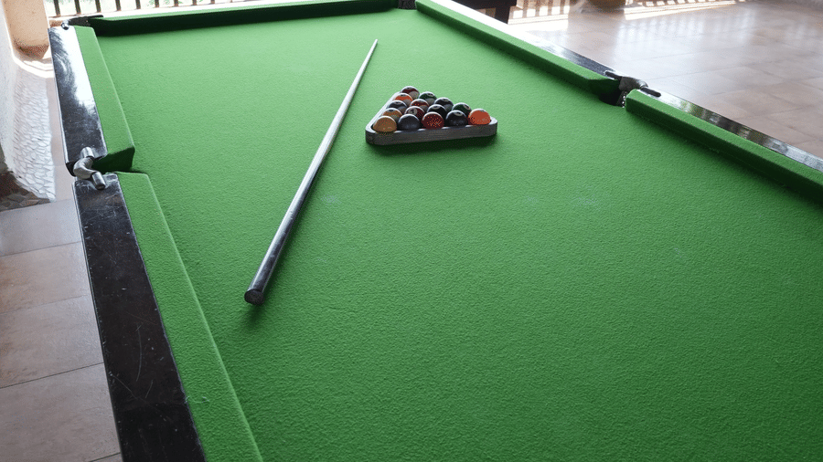A pool table, a cue stick, and billiard balls sit on a covered terrace at Bougainvillea, Alibaug.