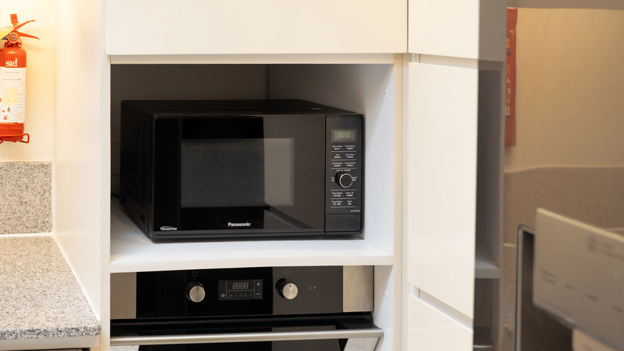 Kitchen area equipped with a microwave, built in oven, and storage cabinets at Central Mansions, Phnom Penh.