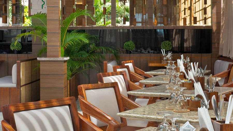 5th Bistro Cafe and Bar at Coral Reef Resort & Spa in Havelock featuring a dining area with outdoor seating, featuring wooden tables and striped chairs. The space is set in a lush garden with ample greenery, creating a comfortable, scenic setting - Coral R