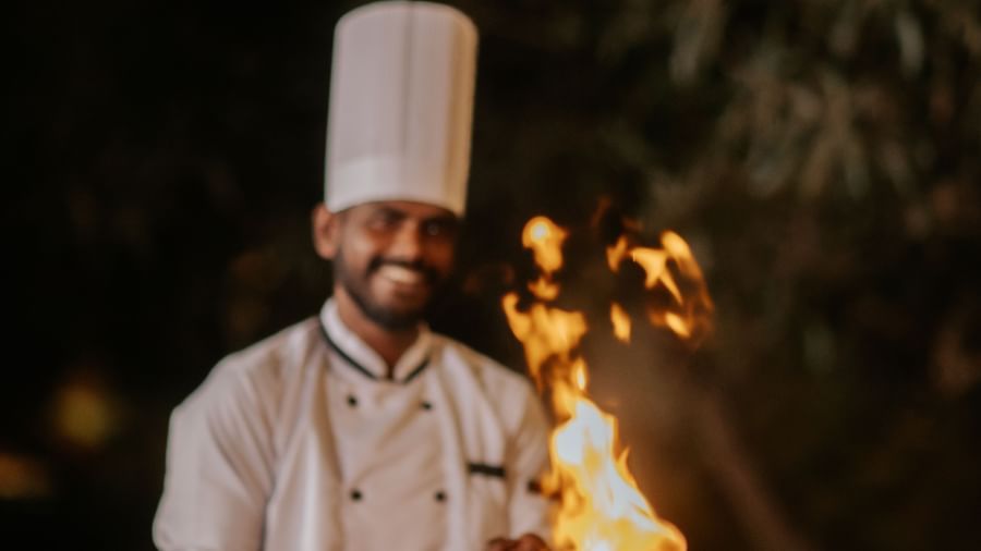 A chef cooking with a wide smile while tossing food on a pan at the Daksh Eden Greens in Sasan Gir, during the night.