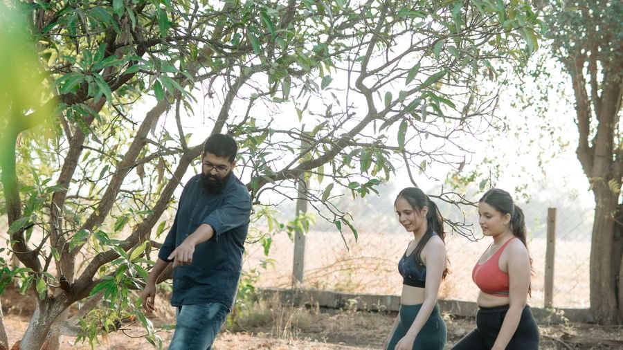 A man pointing towards plants and two women looking at the same spot amidst the farm covered in plants and trees at Daksh Eden Greenz in Sasan Gir.