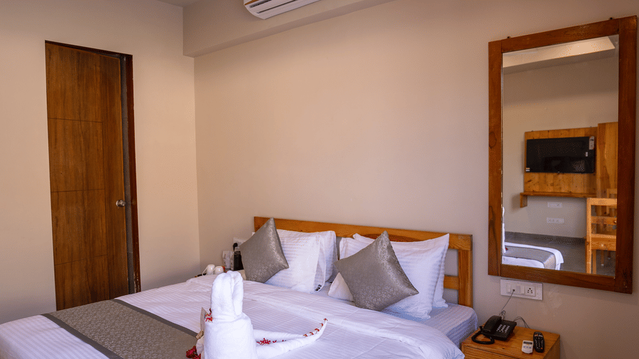 A well-lit double bedroom featuring a wooden bed frame, air conditioning, and a full-length mirror - Daksh The Nirvana Retreat, Pavagadh