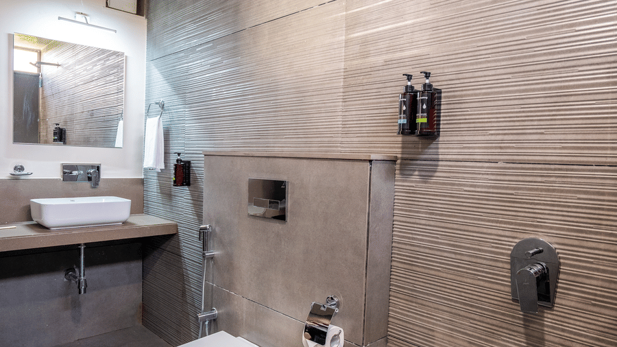 A sleek, modern bathroom with grey stone tiling, a wall-mounted toilet, and contemporary fixtures - Daksh The Nirvana Retreat, Pavagadh