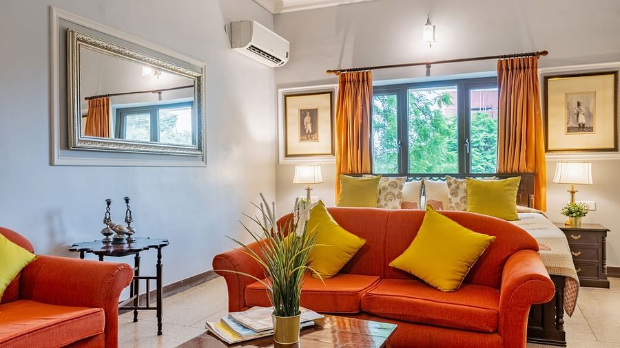 A vibrant living area at Dera Rawatsar, Jaipur, features comfortable sofas, a wooden coffee table on a patterned rug, and glimpses of a cozy bedroom.