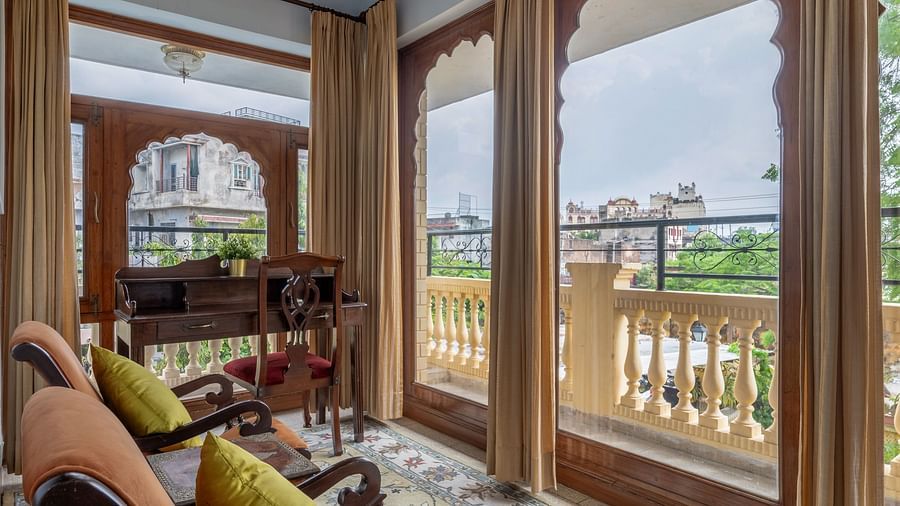A charming sitting area at Dera Rawatsar, Jaipur, offers comfortable chairs, arched doorways with scenic views, and a patterned rug on the floor.