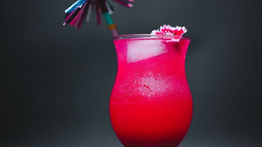 A vibrant pink mocktail served in a curvy glass with a decorative straw and a small paper umbrella, set against a dark background at D Café in Dip Holidays.